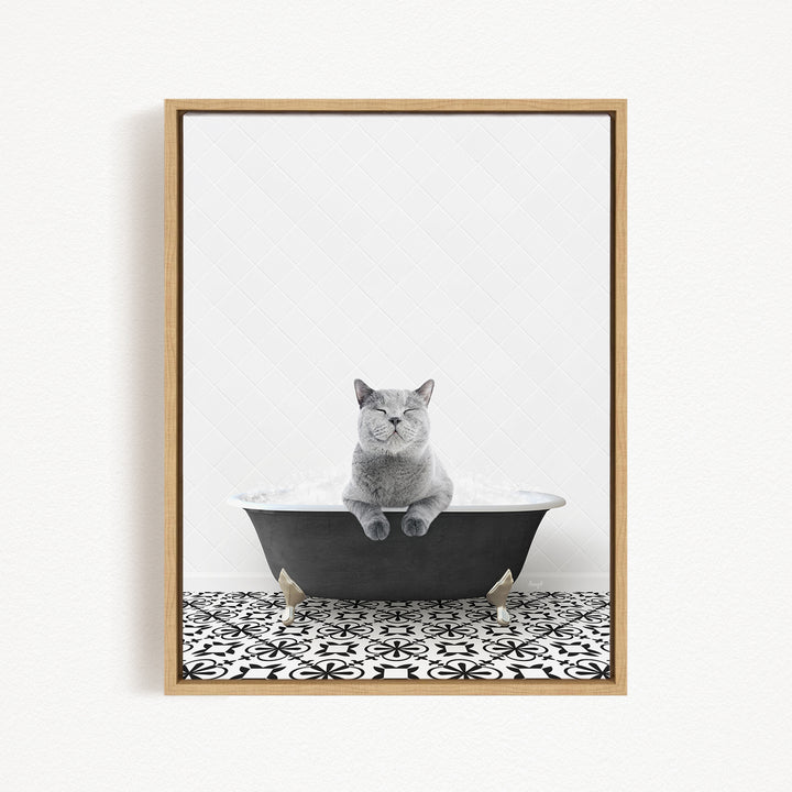 A gray cat sitting in a black bathtub filled with bubbles, with a black and white patterned floor beneath it.