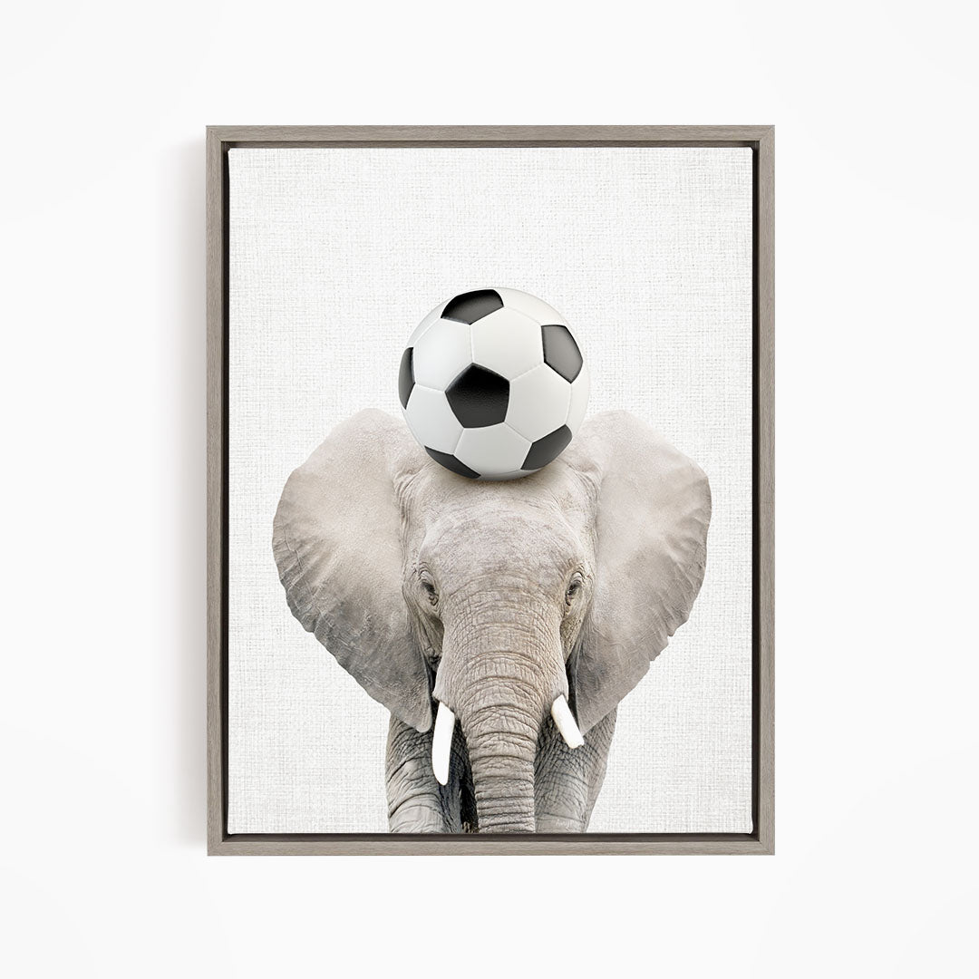 A gray elephant balances a soccer ball on its head, creating a playful and whimsical scene.