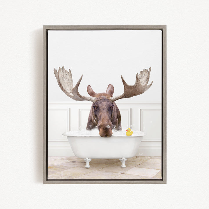 A moose with large antlers is sitting in a white bathtub, with a rubber duck floating in the water.