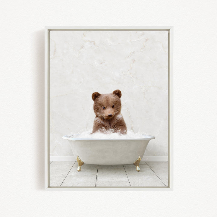 A cute brown bear sitting in a white bathtub filled with bubbles, looking directly at the camera.