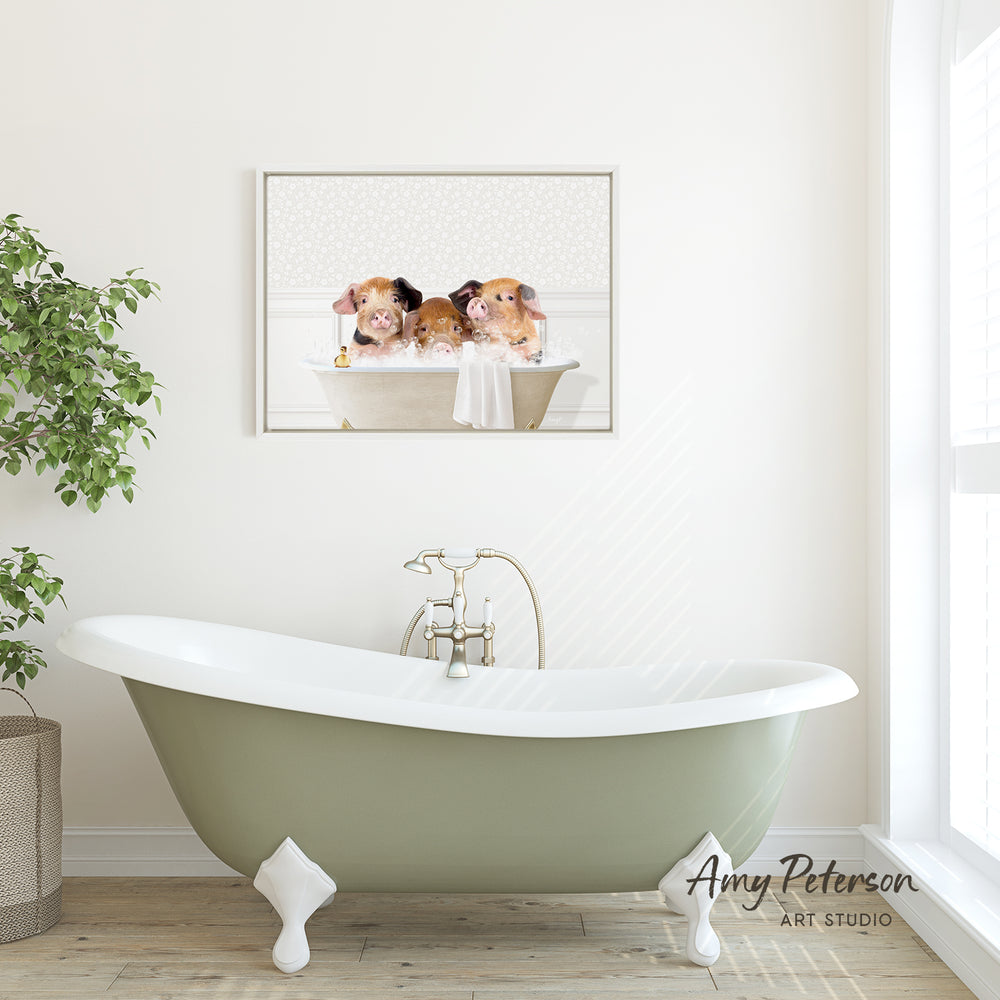 A framed image of three adorable pigs sitting in a bathtub is displayed on the wall above a green clawfoot bathtub in a bright, white-walled bathroom.