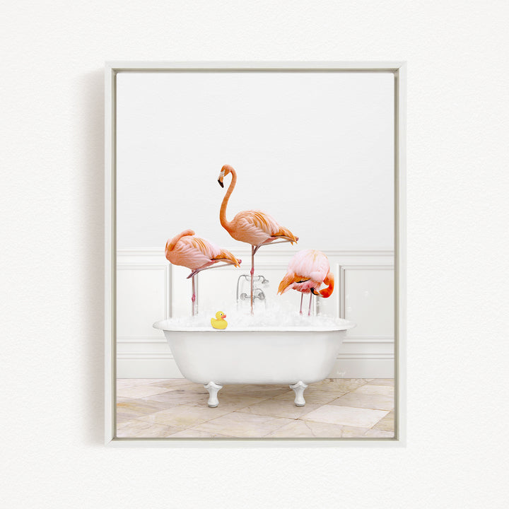 A framed image depicting three flamingos standing in a white bathtub filled with water, with a yellow rubber duck floating in the water.