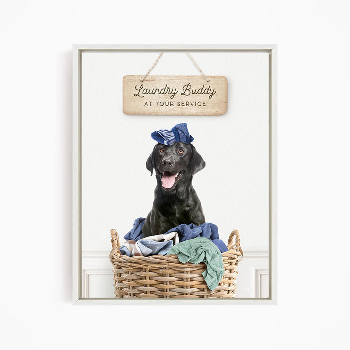 A black dog wearing a blue hat sits in a wicker laundry basket, with a wooden sign above that reads "Laundry Buddy at your service".