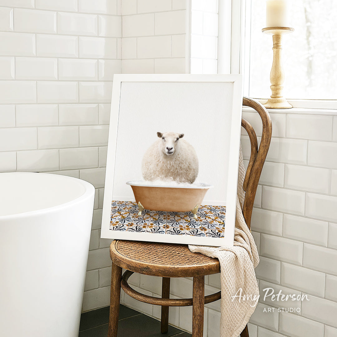 A framed image of a sheep sitting in a bathtub is displayed on a wooden chair in a bathroom setting.