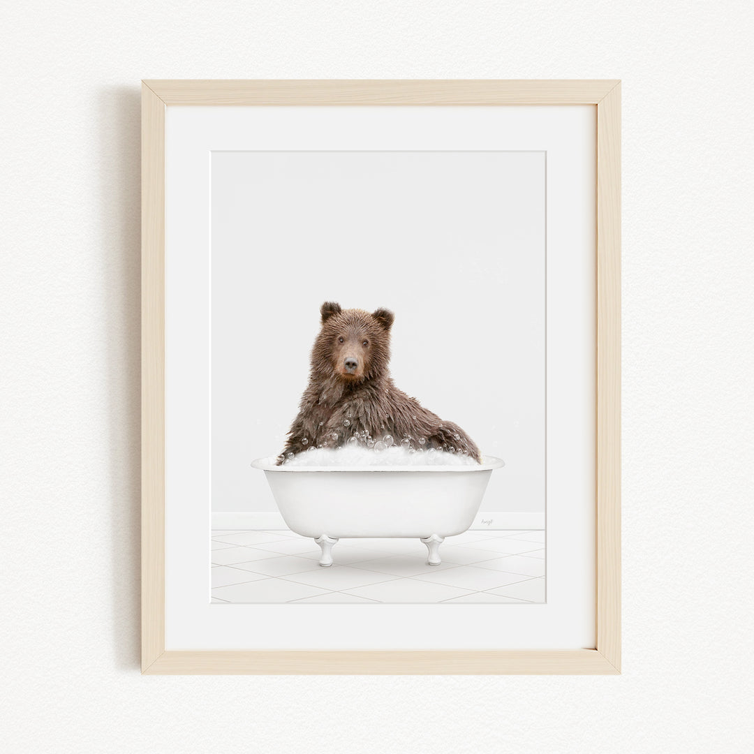 A brown bear sitting in a white bathtub filled with bubbles, looking directly at the camera.