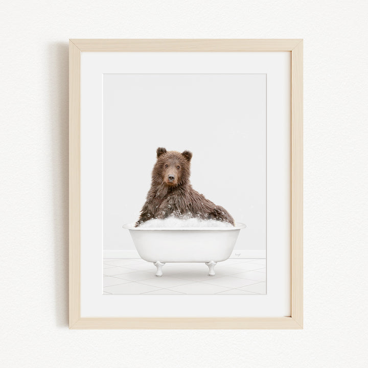 A brown bear sitting in a white bathtub filled with bubbles, looking directly at the camera.