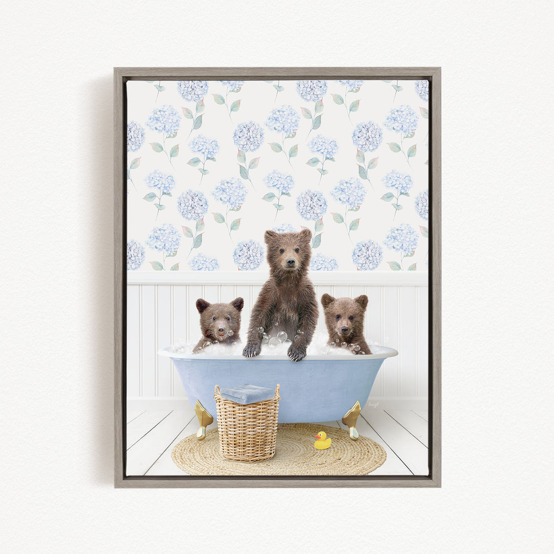 A framed image depicting three bears sitting in a bathtub, with a blue floral pattern on the wall behind them.