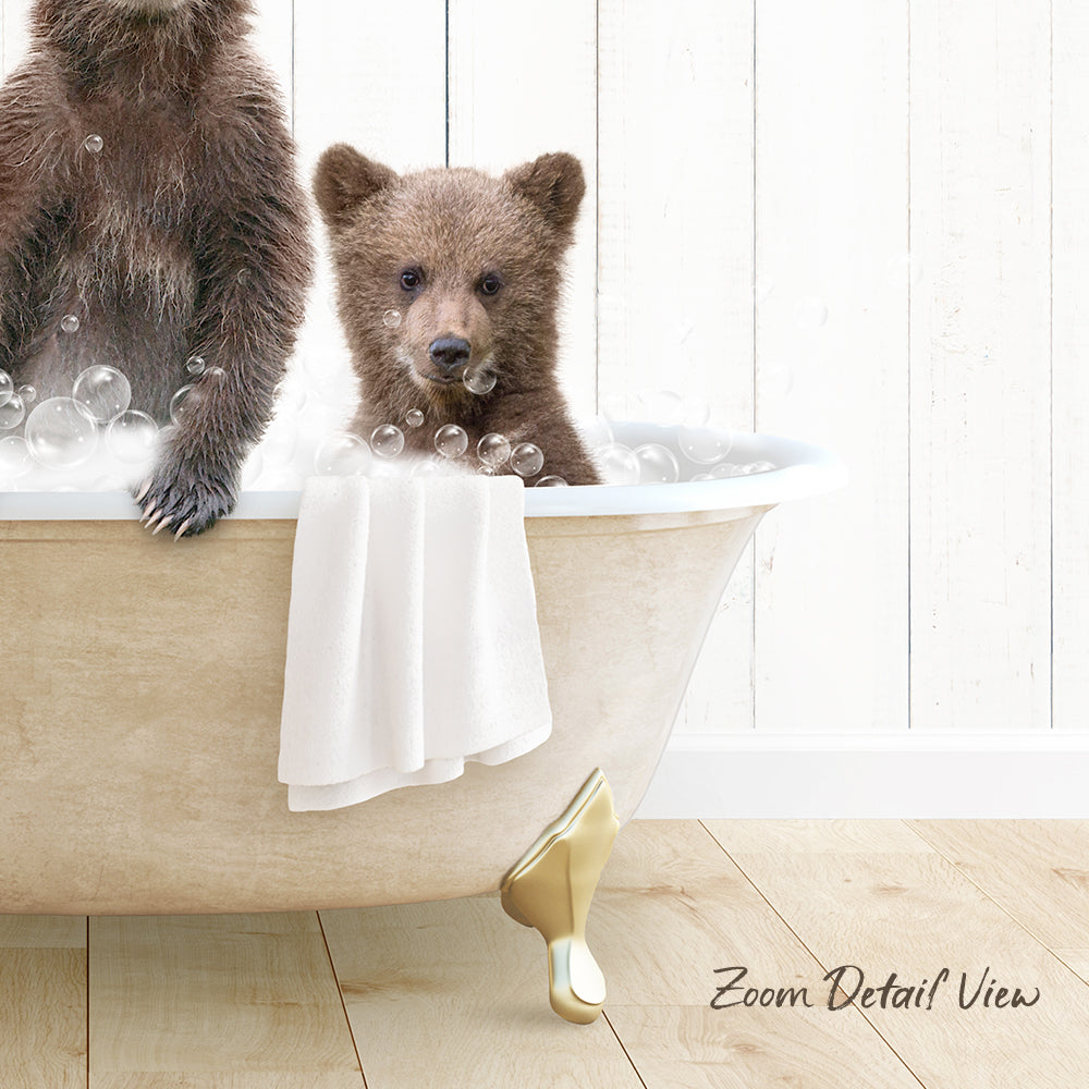 A baby bear sitting in a bathtub filled with bubbles, with a towel draped over the side of the tub.