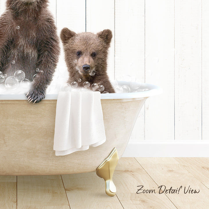 A baby bear sitting in a bathtub filled with bubbles, with a towel draped over the side of the tub.