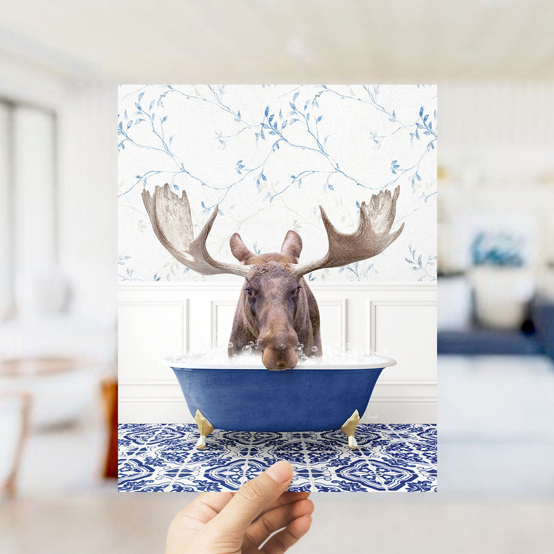 A moose with large antlers is sitting in a blue bathtub, surrounded by a patterned tile floor and a floral wallpaper.