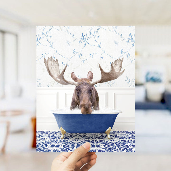 A moose with large antlers is sitting in a blue bathtub, surrounded by a patterned tile floor and a floral wallpaper.