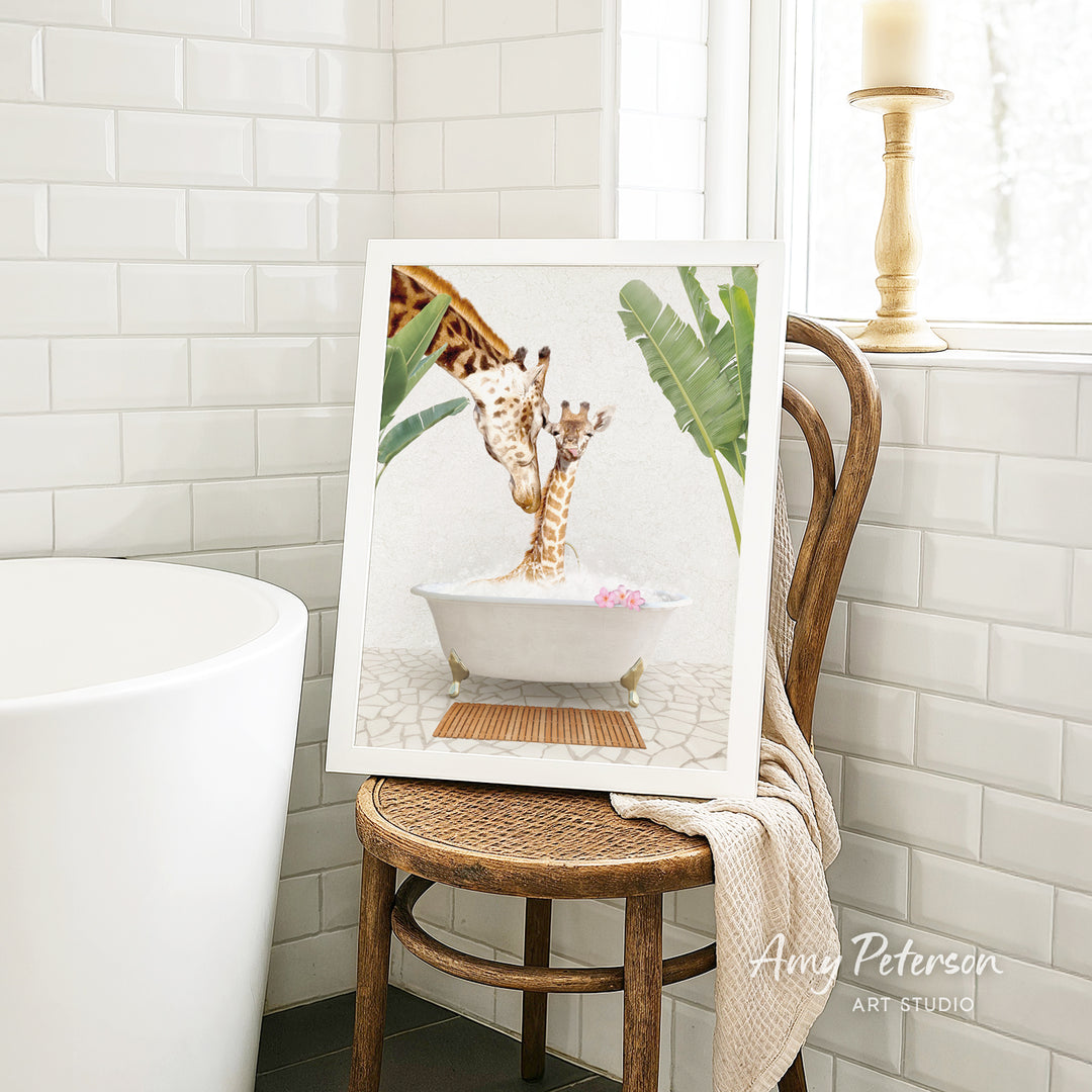 A framed image of two giraffes sitting in a bathtub, surrounded by tropical plants, is displayed on a wooden chair in a bathroom setting.
