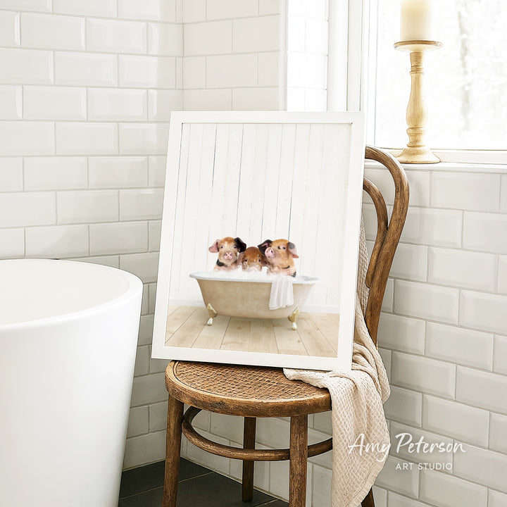 A framed image of two adorable puppies sitting in a bathtub, with a towel draped over the side of the tub, is displayed on a wooden chair in a bathroom setting.