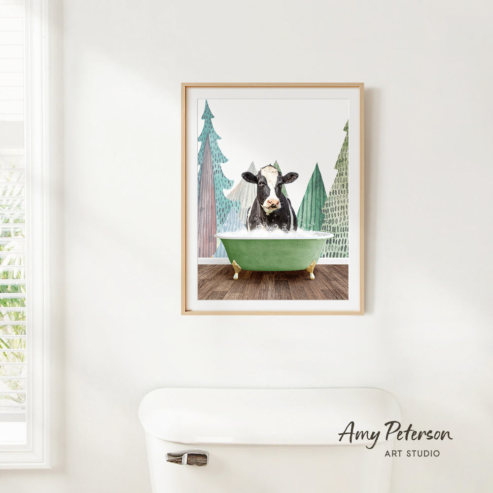 A framed print of a cow sitting in a green bathtub, surrounded by trees, is hanging on a white wall.