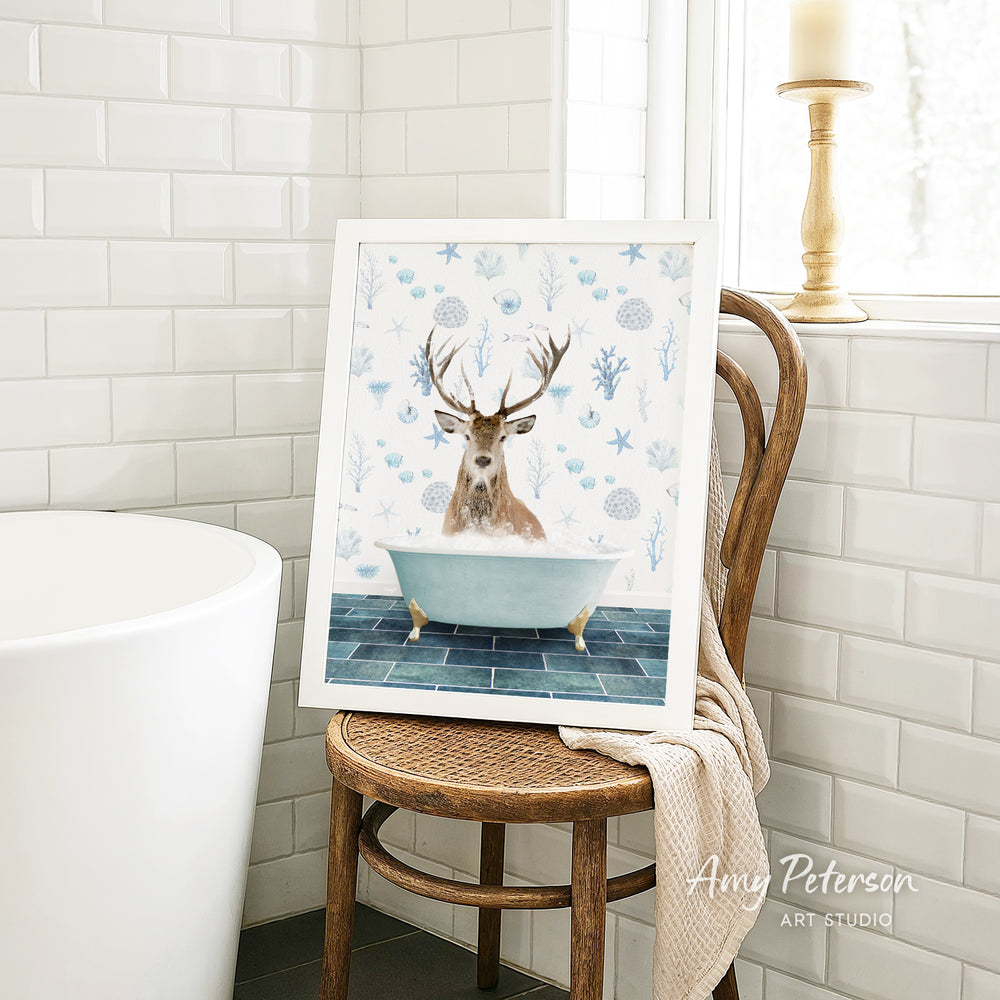 A framed image of a deer sitting in a bathtub, surrounded by blue and white floral patterns, is displayed on a wooden chair in a bathroom setting.