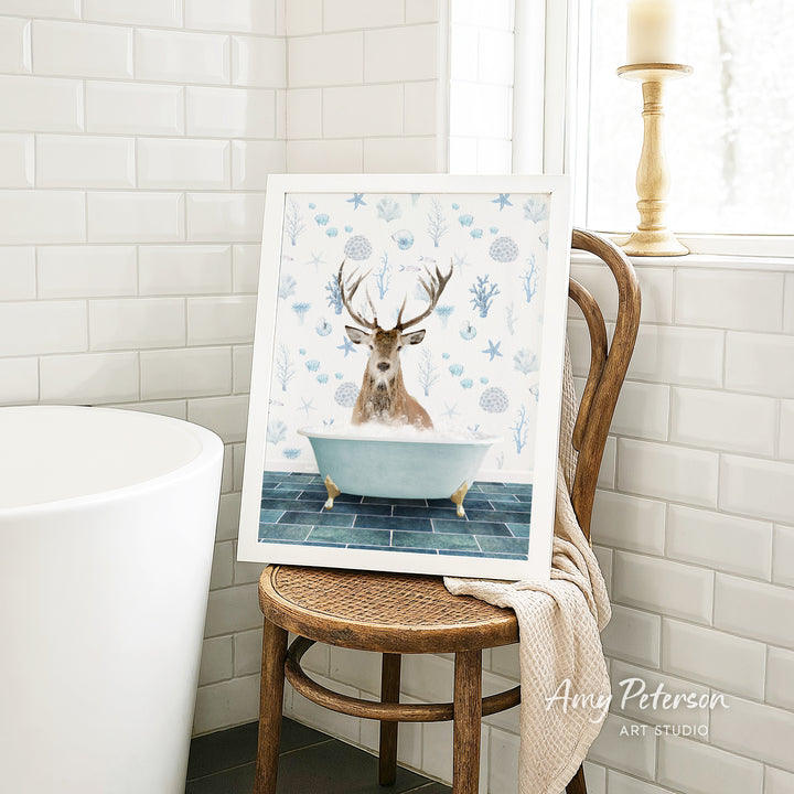 A framed image of a deer sitting in a bathtub, surrounded by blue and white floral patterns, is displayed on a wooden chair in a bathroom setting.