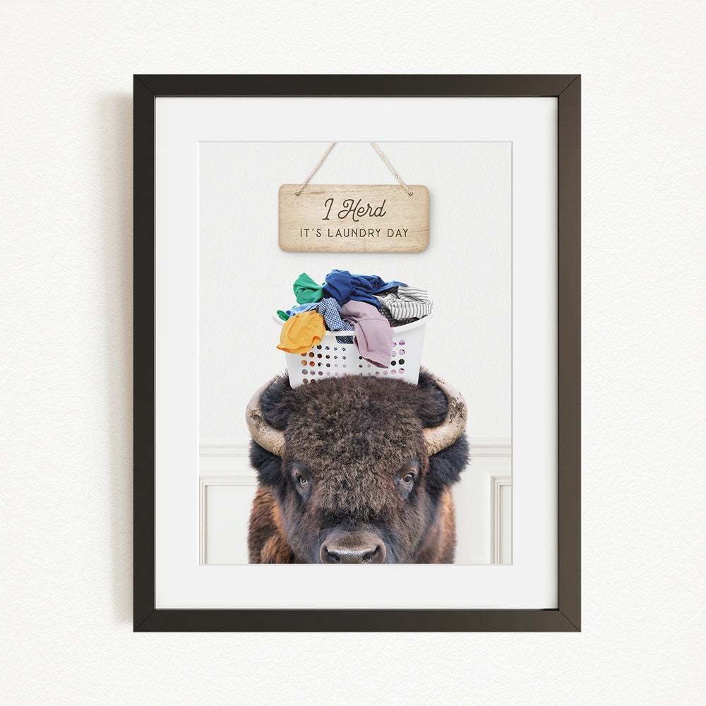 A buffalo with a basket of laundry on its head, accompanied by a wooden sign that says "I herd, it's laundry day".