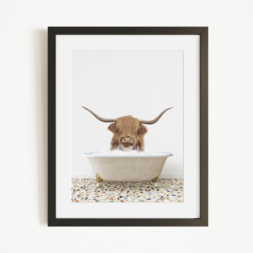 A framed image depicting a Highland cow with long horns sitting in a bathtub filled with water.