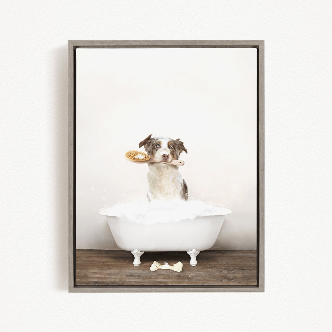 A dog sitting in a white bathtub, holding a brush in its mouth, with a wooden floor and a white wall in the background.