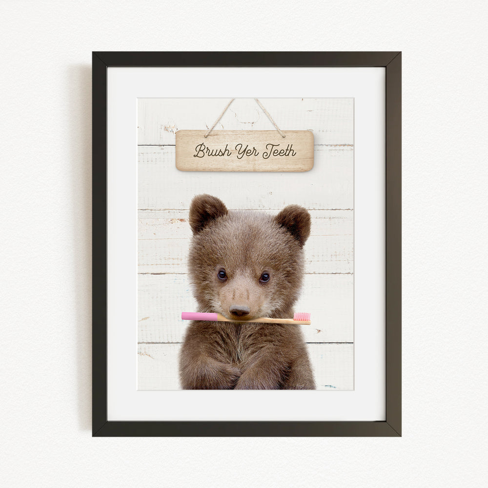A cute brown bear holding a pink toothbrush in front of a wooden sign that says "Brush Your Teeth".