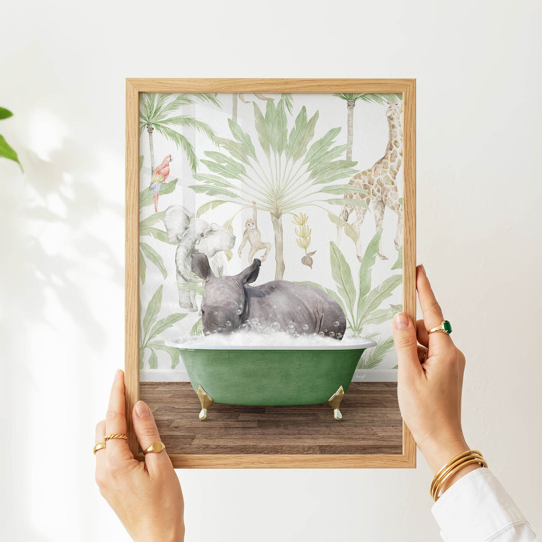 A person's hands are holding a framed picture of a rhinoceros sitting in a green bathtub, surrounded by tropical foliage.