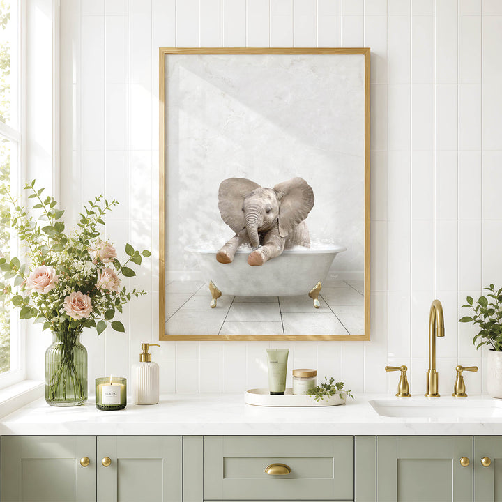 A framed image of a baby elephant sitting in a bathtub is displayed on the wall above a bathroom counter with various toiletries and a vase of flowers.