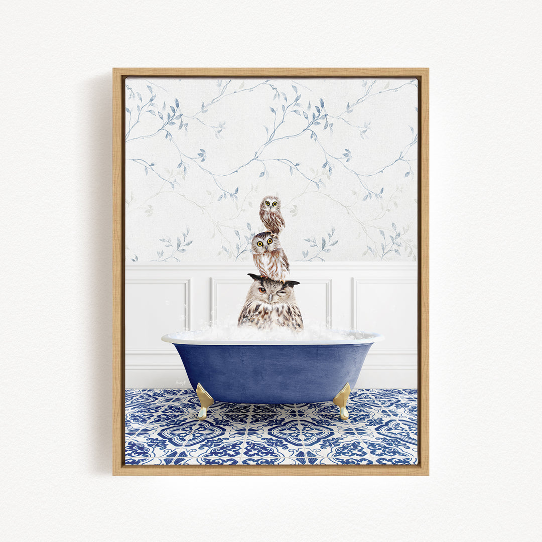 A framed image depicting a group of owls sitting in a blue bathtub, with a patterned tile floor and a floral wallpaper in the background.