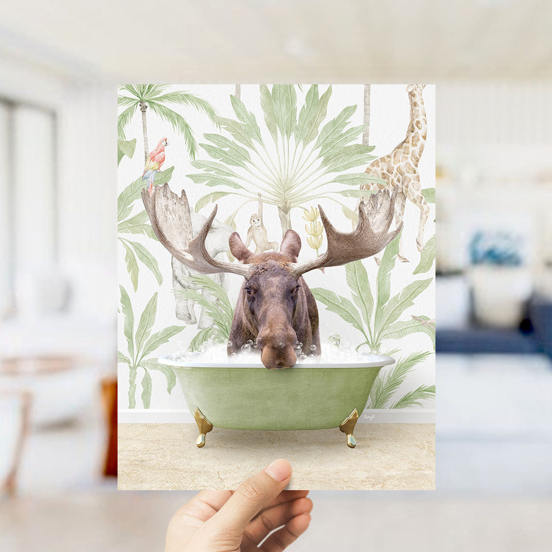A hand holds up a collage of an image featuring a moose in a bathtub surrounded by tropical plants and animals, including a giraffe and a parrot.