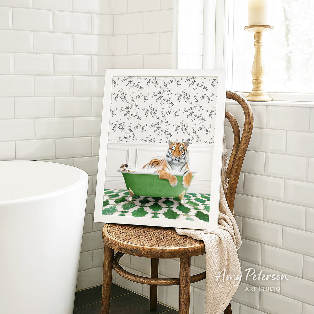 A framed print of a tiger sitting in a green bathtub is displayed on a wooden chair in a bathroom setting.