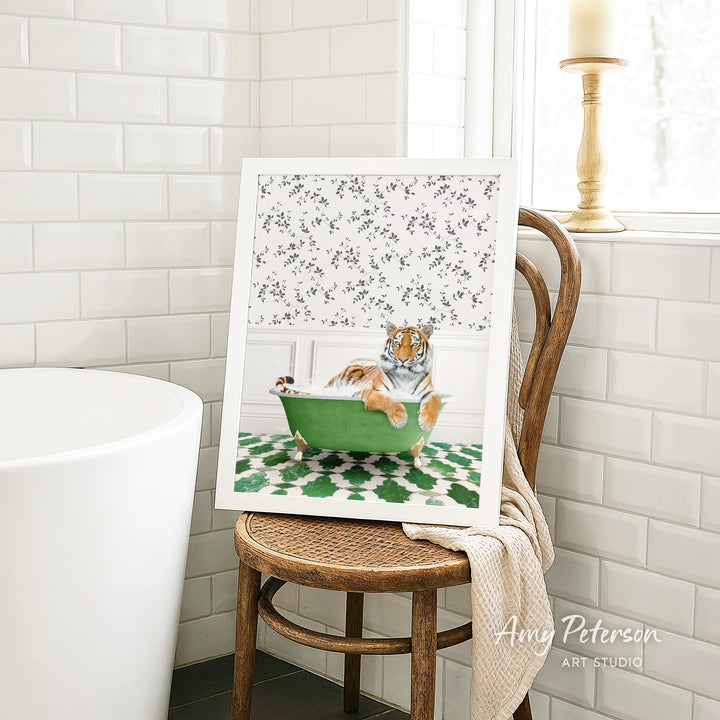 A framed print of a tiger sitting in a green bathtub is displayed on a wooden chair in a bathroom setting.