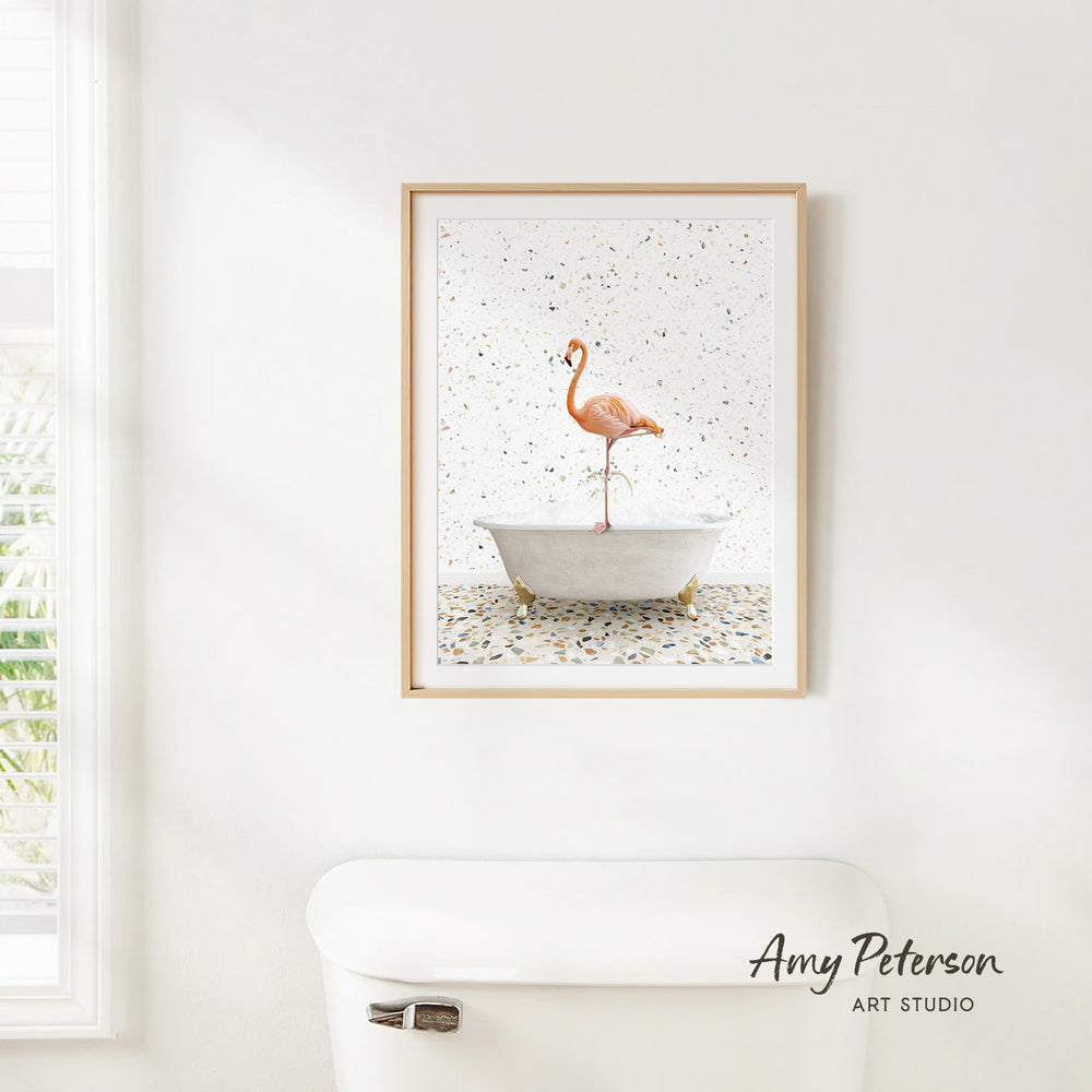 A framed painting of a flamingo standing in a bathtub is hanging on a white wall in a bathroom.