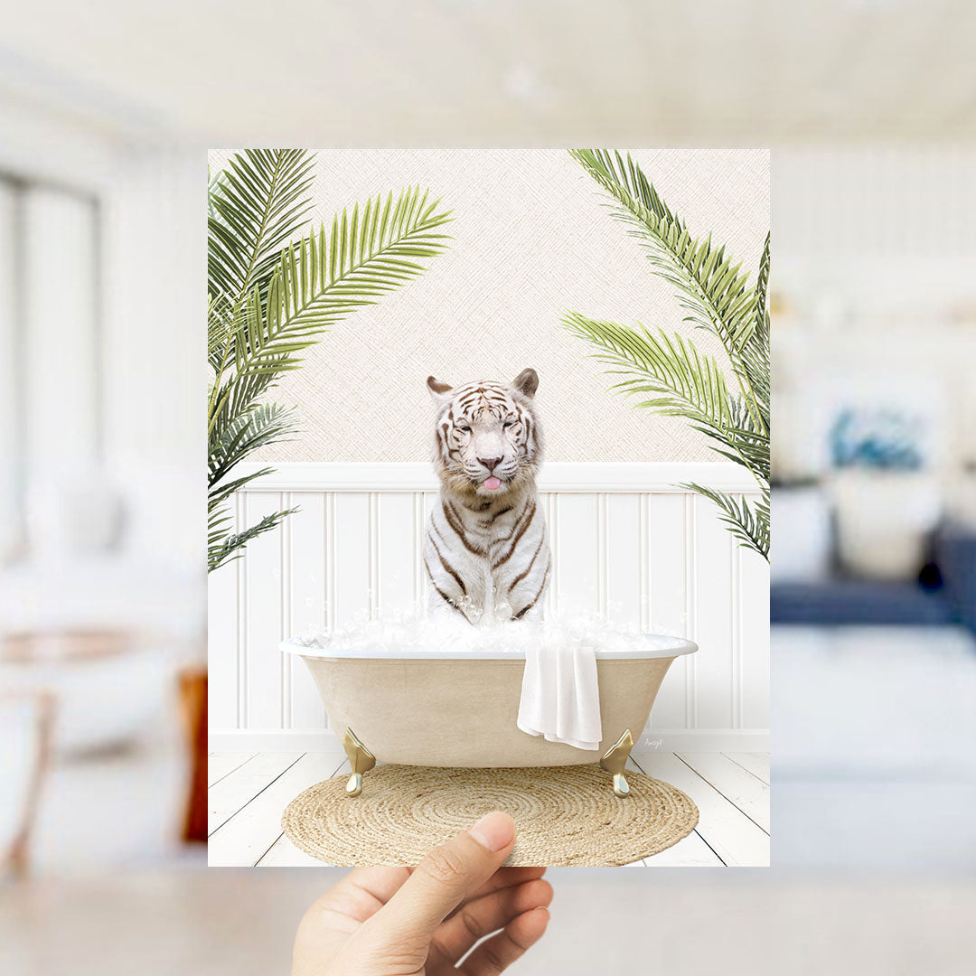 A hand holds up a framed image depicting a white tiger sitting in a bathtub filled with water, surrounded by green palm leaves.
