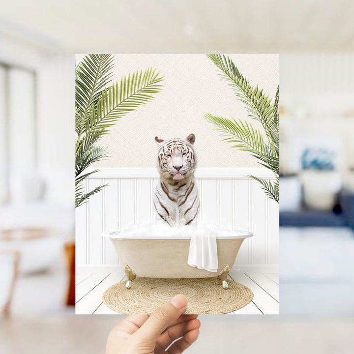 A hand holds up a framed image depicting a white tiger sitting in a bathtub filled with water, surrounded by green palm leaves.