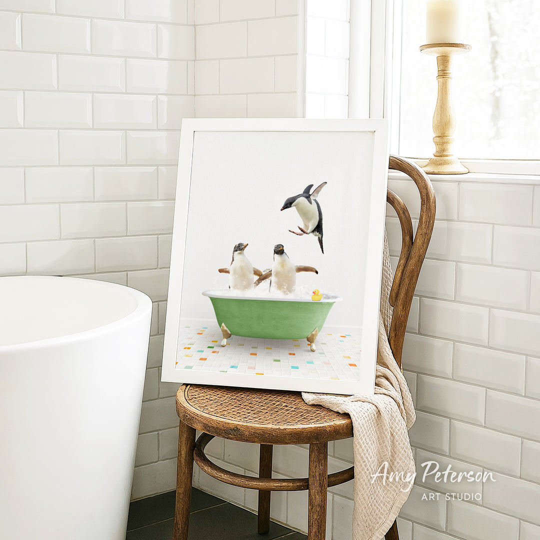 A framed image of two penguins sitting in a green bathtub, surrounded by colorful tiles, is displayed on a wooden chair in a bathroom setting.