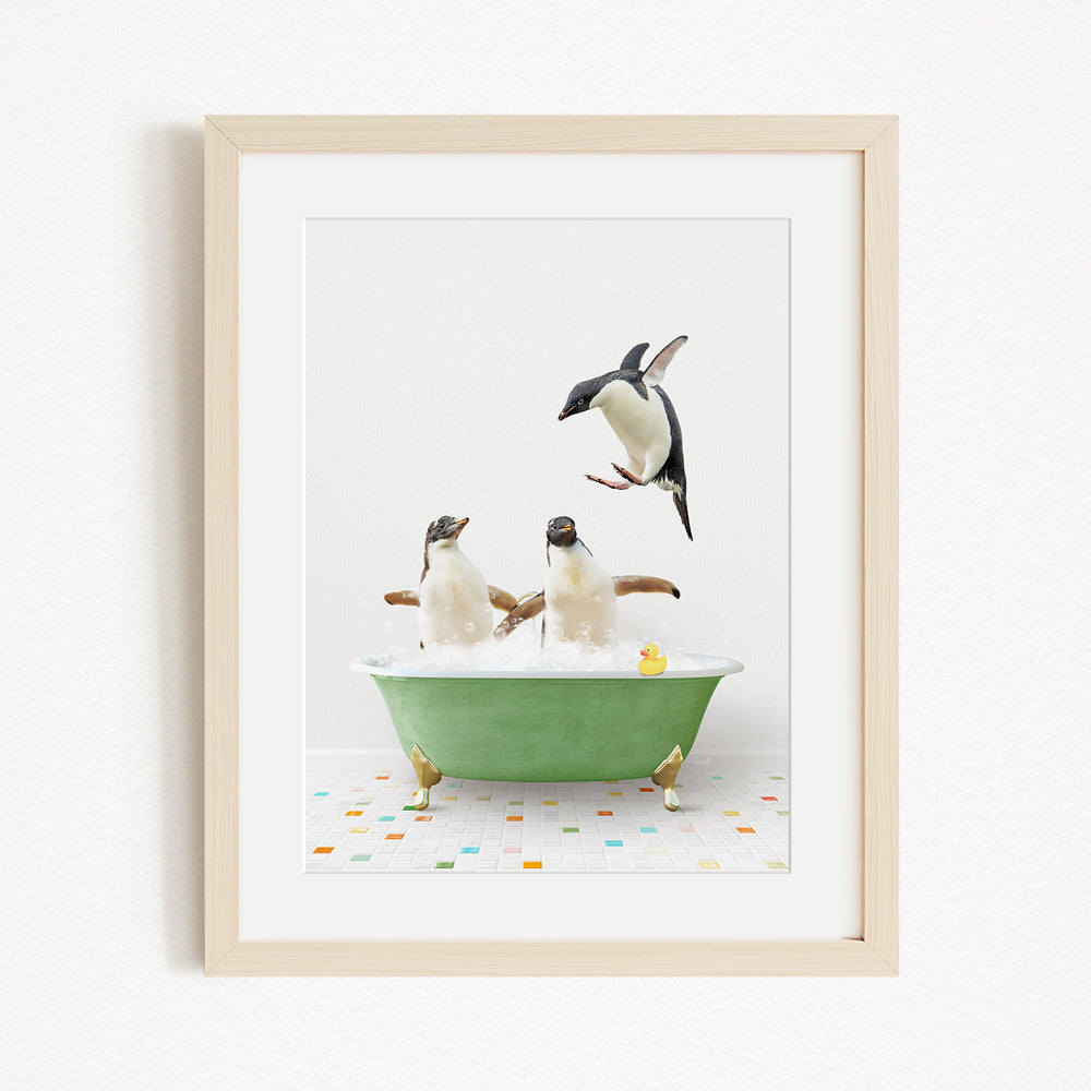 A framed image depicting two penguins sitting in a green bathtub, with one penguin standing on its hind legs and another penguin sitting on its belly, while a third penguin jumps into the tub.