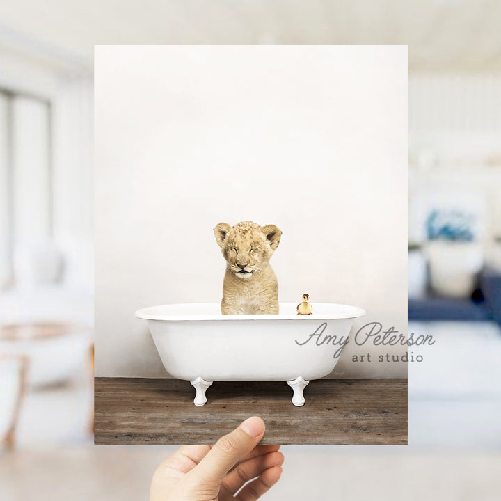 a hand holding a photo of a baby lion in a bathtub