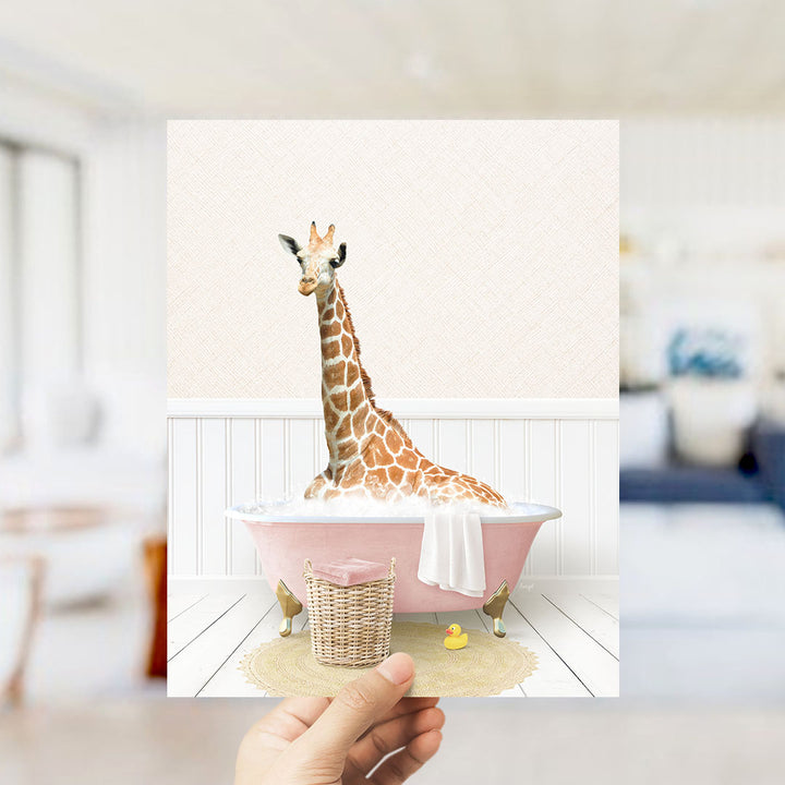 A giraffe sitting in a pink bathtub filled with bubbles, surrounded by a yellow rubber duck and a white towel.
