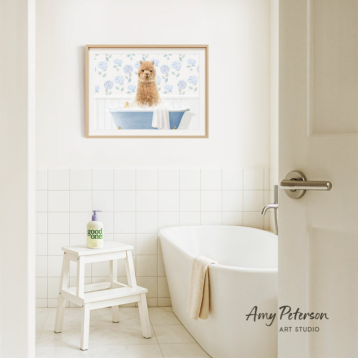 A framed painting of a dog sitting in a bathtub is hanging on a white tiled wall above a white bathtub in a bathroom.