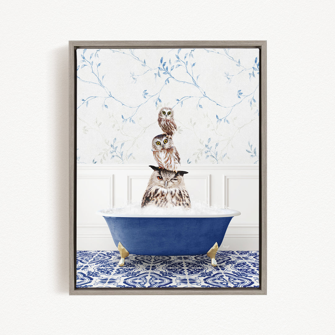 A framed image depicting an owl sitting in a blue bathtub, surrounded by a patterned tile floor and a white wall with blue floral wallpaper.