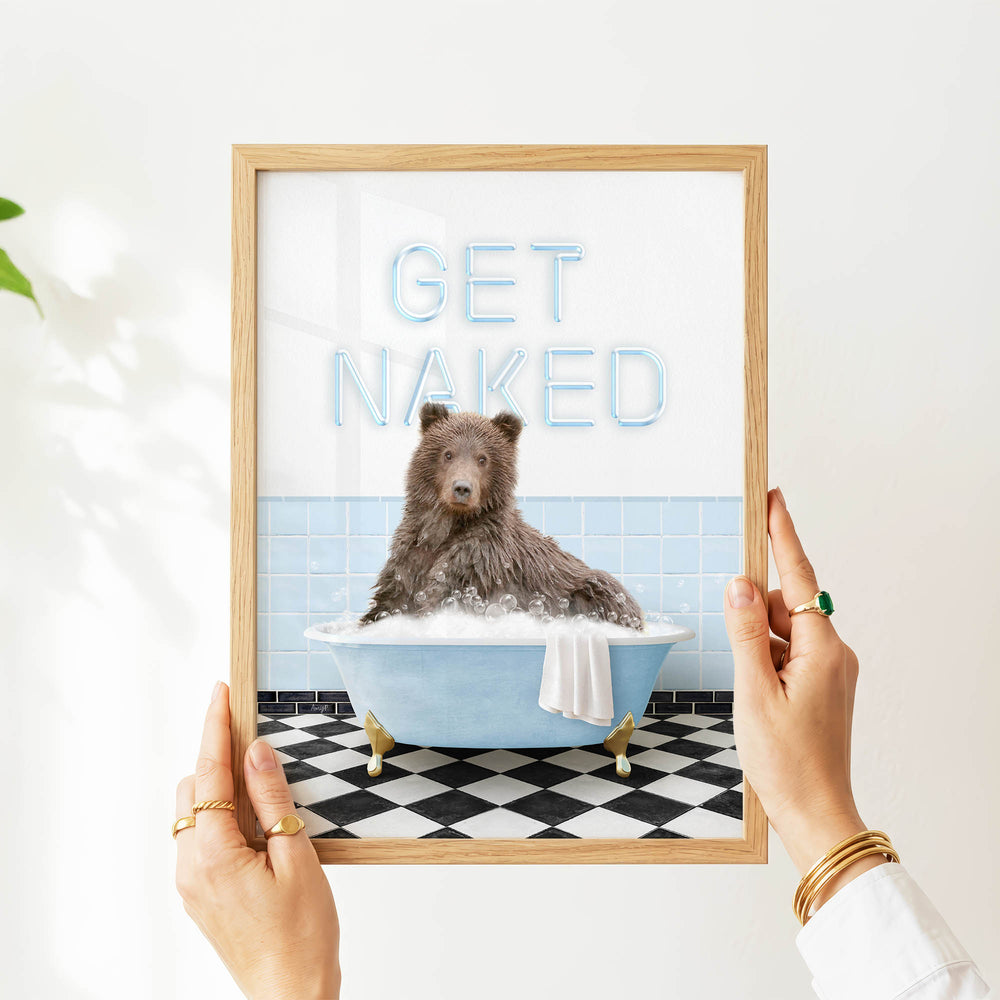 A person's hands are holding a framed picture of a bear sitting in a bathtub with the text "GET NAKED" written on it.
