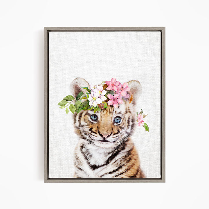 A young tiger cub wearing a floral crown on its head, with its eyes looking directly at the camera.