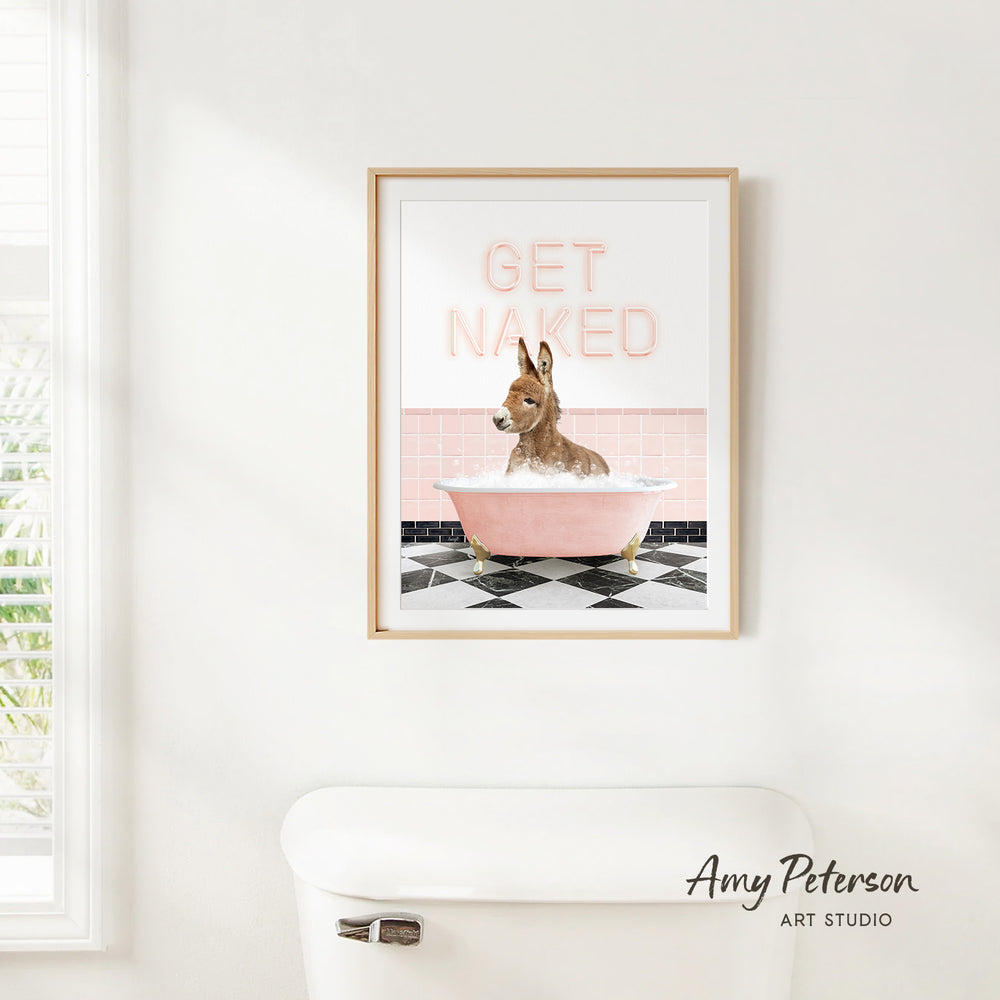A framed print of a dog sitting in a pink bathtub with the text "GET NAKED" on it, hanging on a white wall.