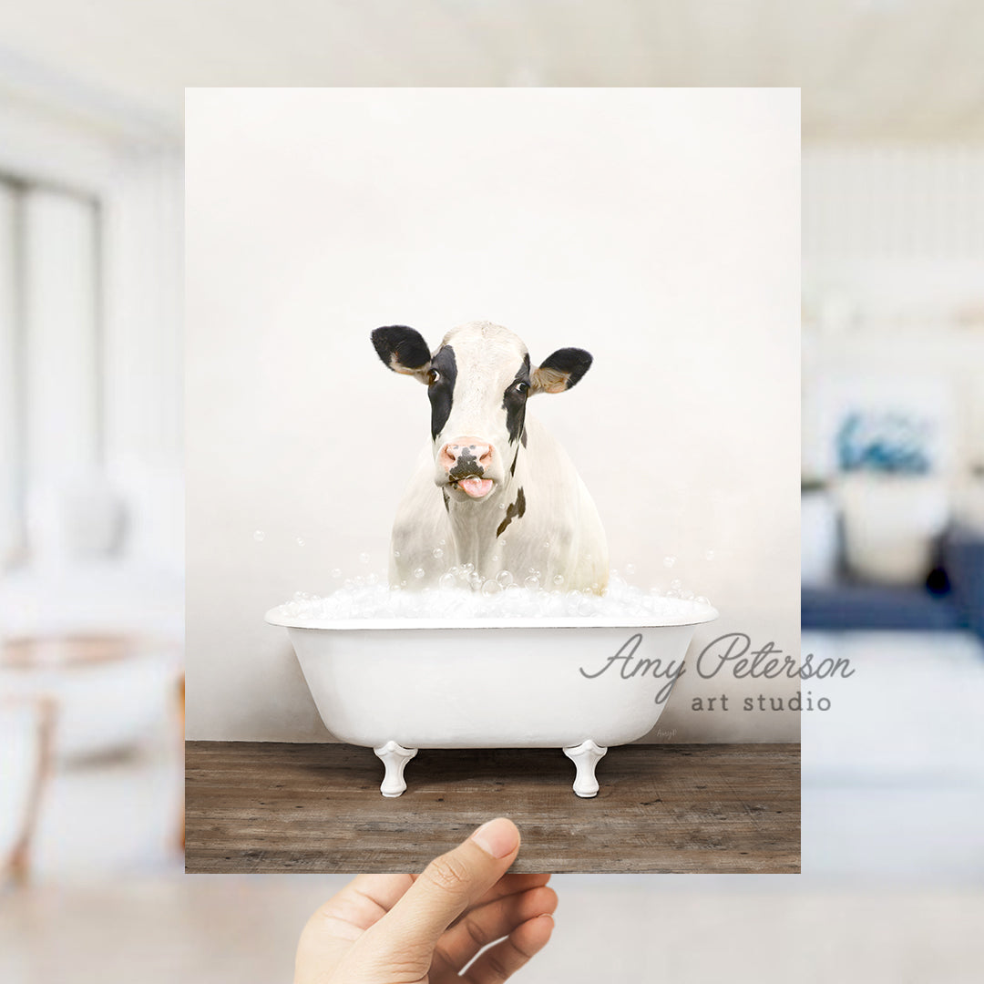 a person holding up a picture of a cow in a bathtub