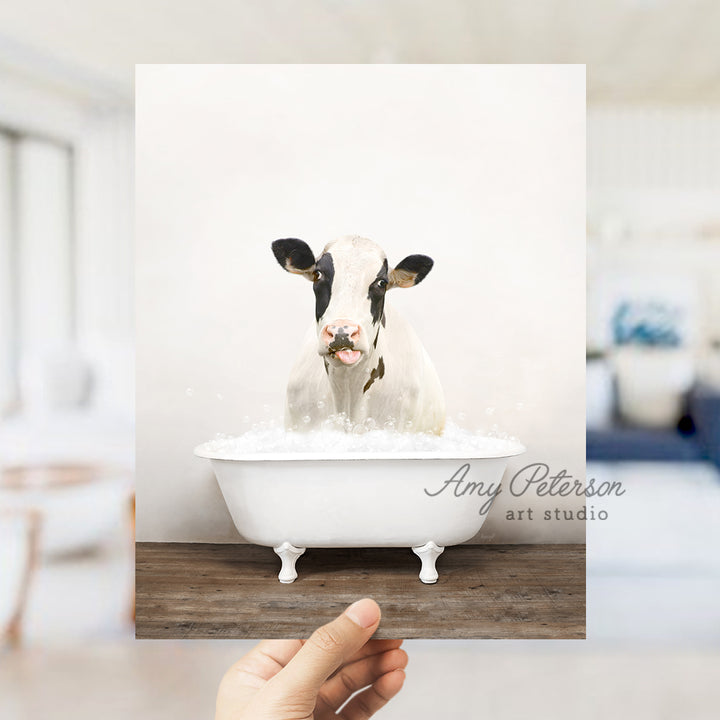 a person holding up a picture of a cow in a bathtub