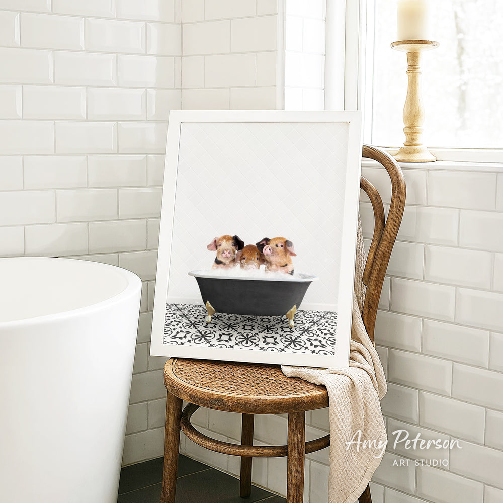 A framed image of two small dogs sitting in a bathtub, with a towel draped over the back of a wooden chair in a bathroom setting.