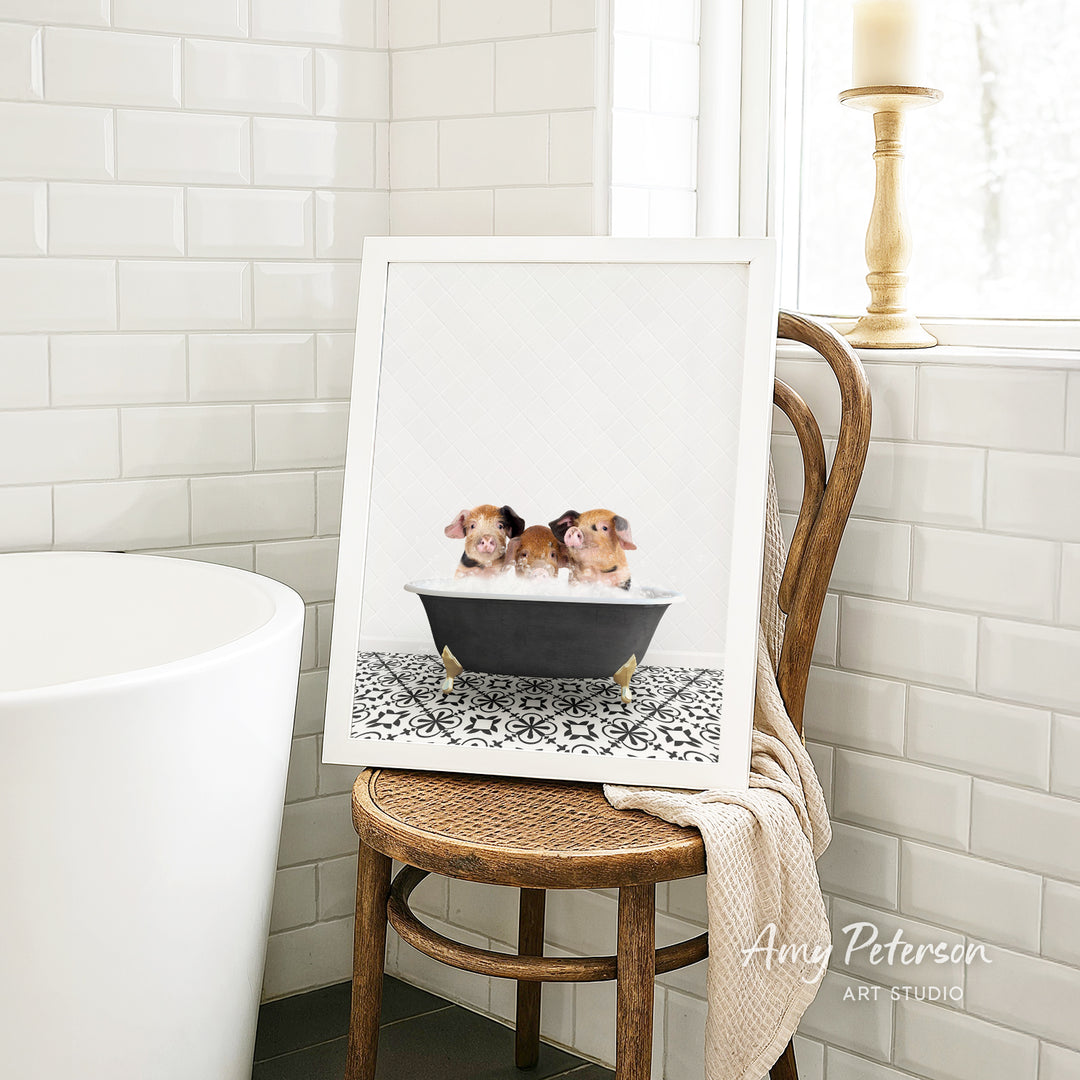 A framed image of two small dogs sitting in a bathtub, with a towel draped over the back of a wooden chair in a bathroom setting.