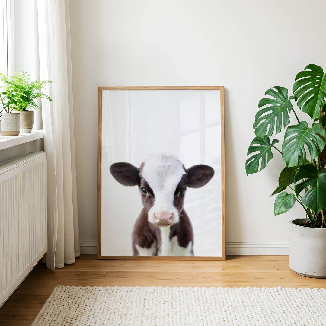 a framed photograph of a cow's face, which is the main focus of the scene. The cow is standing in front of a white wall, and there are two potted plants in the room, one on the left side and the other on the right side.