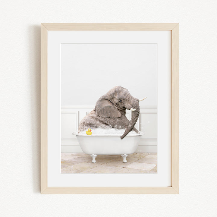 A gray elephant is sitting in a white bathtub, with a yellow rubber duck floating in the water.