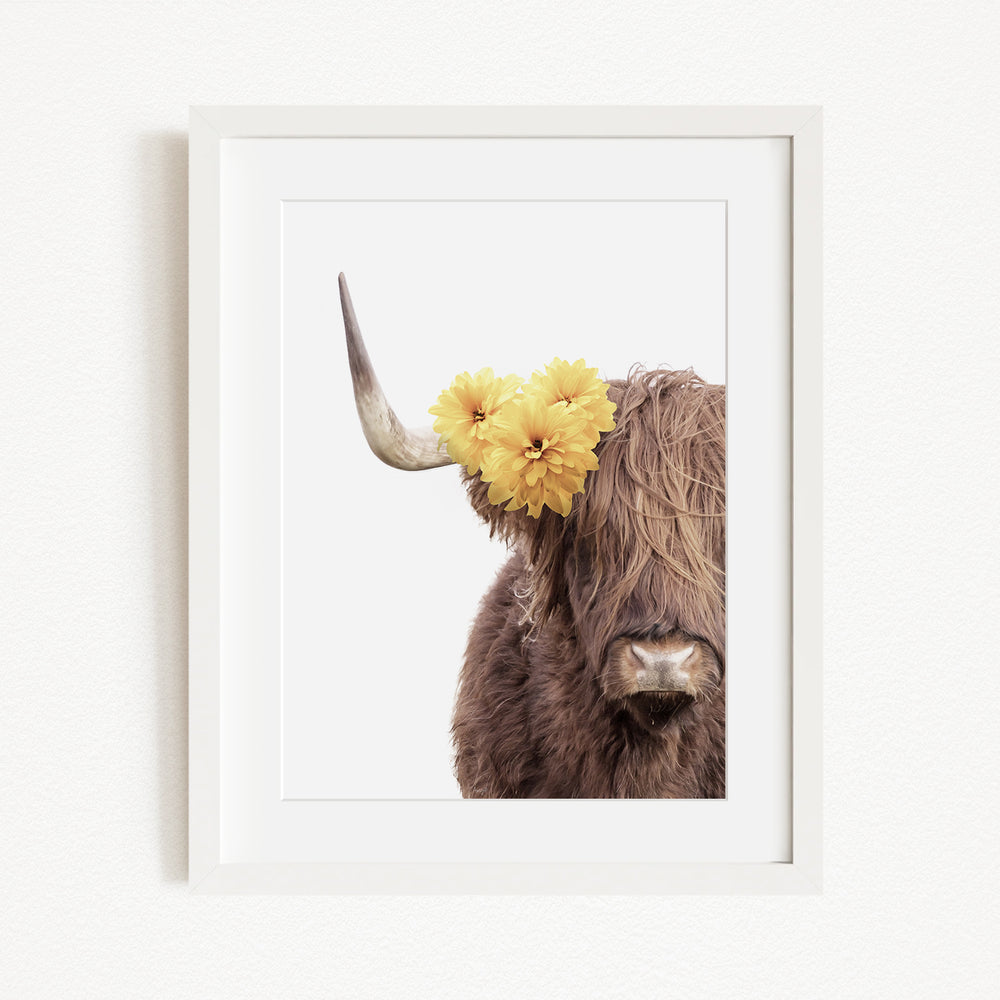 A framed image of a brown cow with yellow flowers on its horns.