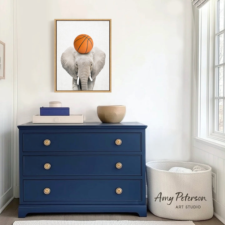 a blue dresser with a framed picture of an elephant holding a basketball on its head, placed above it. The dresser has three drawers and a white basket on the floor next to it.
